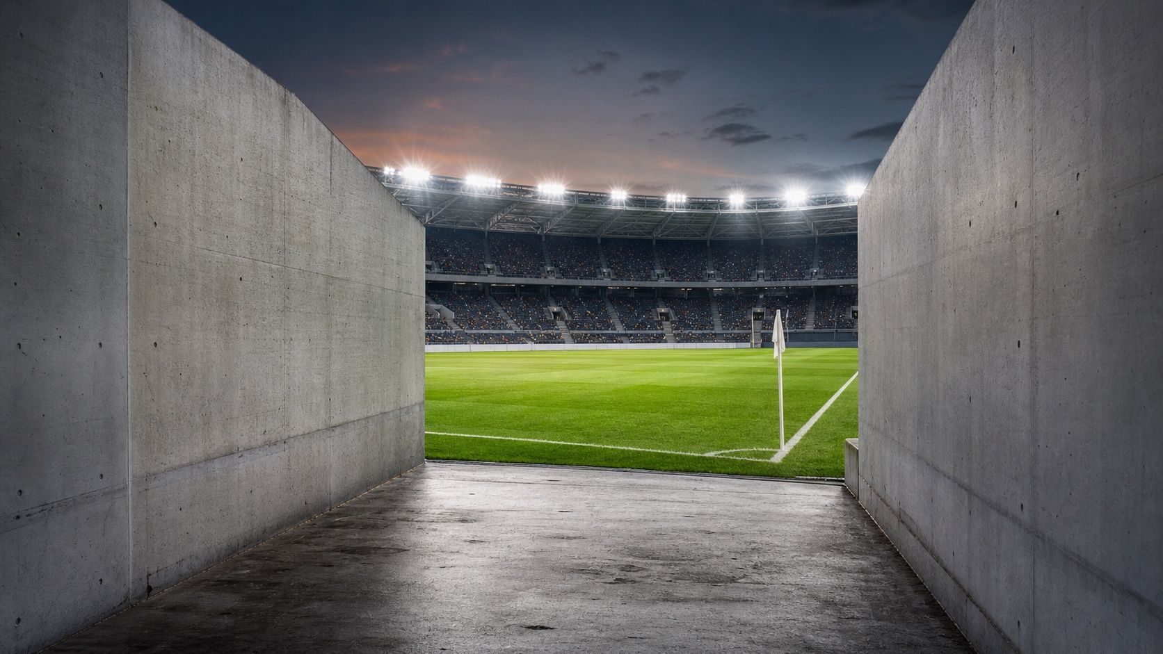 A concrete players' tunnel opening onto a floodlit football pitch